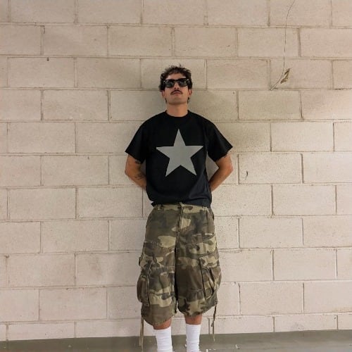O Lucas de t-shirt com uma estrela, encostado a uma parede de blocos.