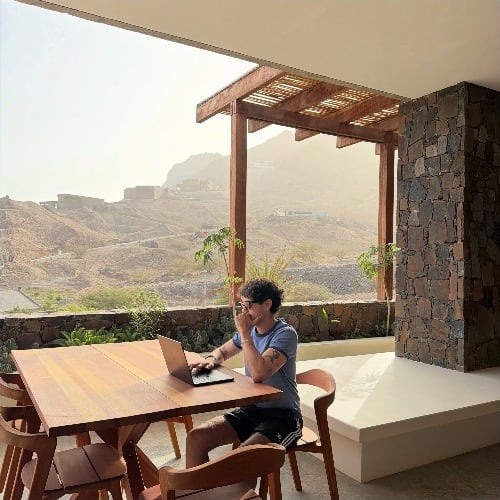 O Lucas a trabalhar ao portátil num terraço, com montanhas ao fundo.