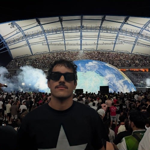 O Lucas num concerto, de óculos escuros, com o palco atrás.